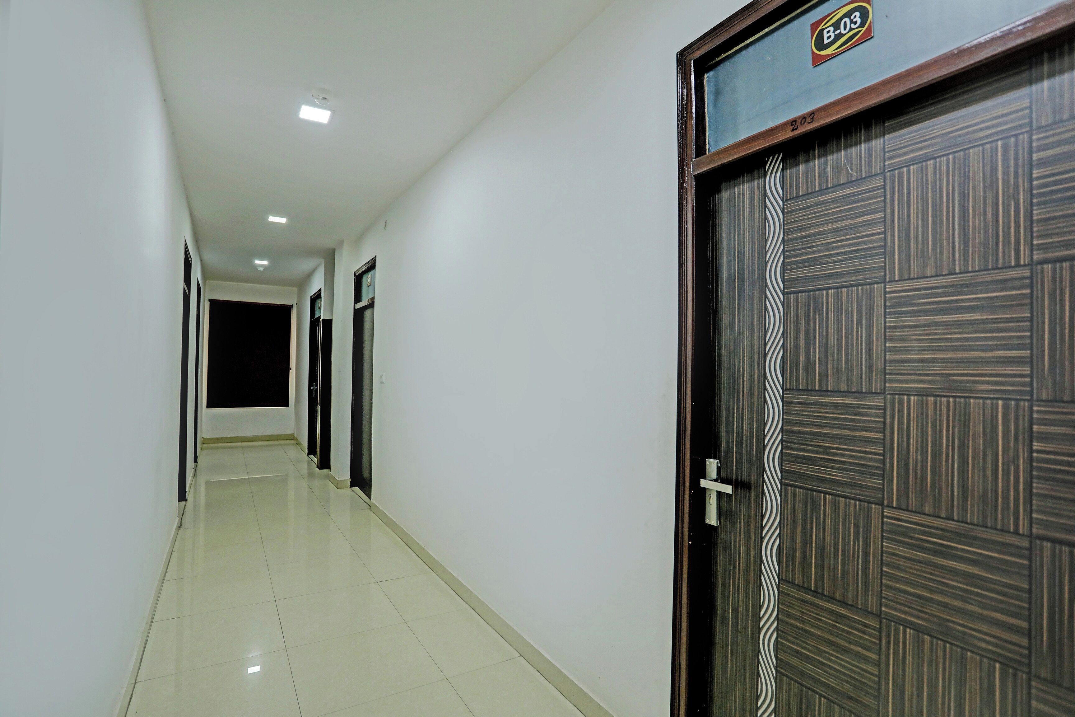 Un pasillo con suelo de baldosas, una puerta con panel decorativo e iluminación empotrada en el techo.