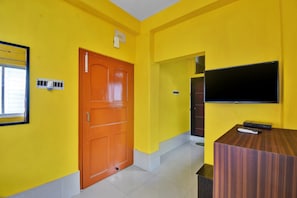 A room with yellow walls, a wooden door, a flat-screen TV mounted on the wall, and a small table with a remote control. - Hotel O Palace (Kolkata)