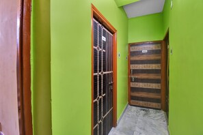 Un pasillo con paredes verdes y dos puertas, una con reja metálica y otra con panel de madera.