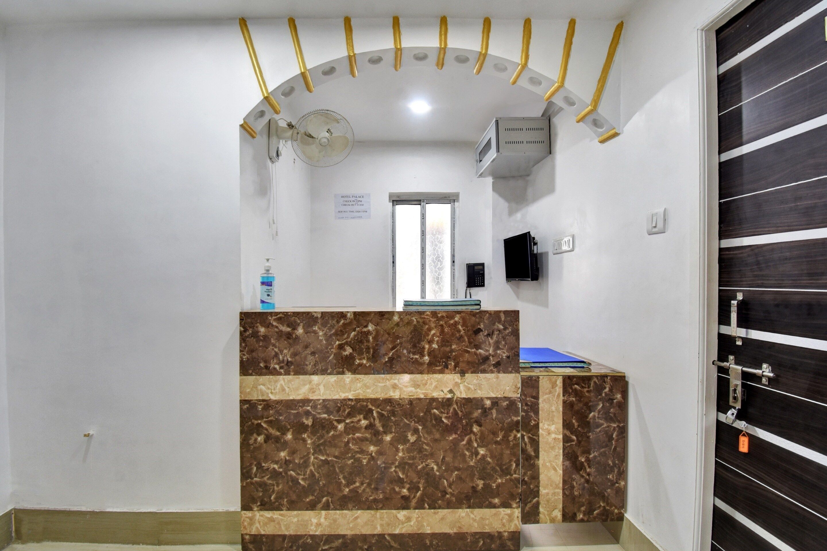 A hotel reception area with a marble counter, a reception desk, a wall-mounted TV, and a door with a security lock.