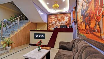 Un espace d’accueil avec un escalier en marbre, un comptoir de réception portant l’inscription « OYO », un lustre et une grande fresque murale.