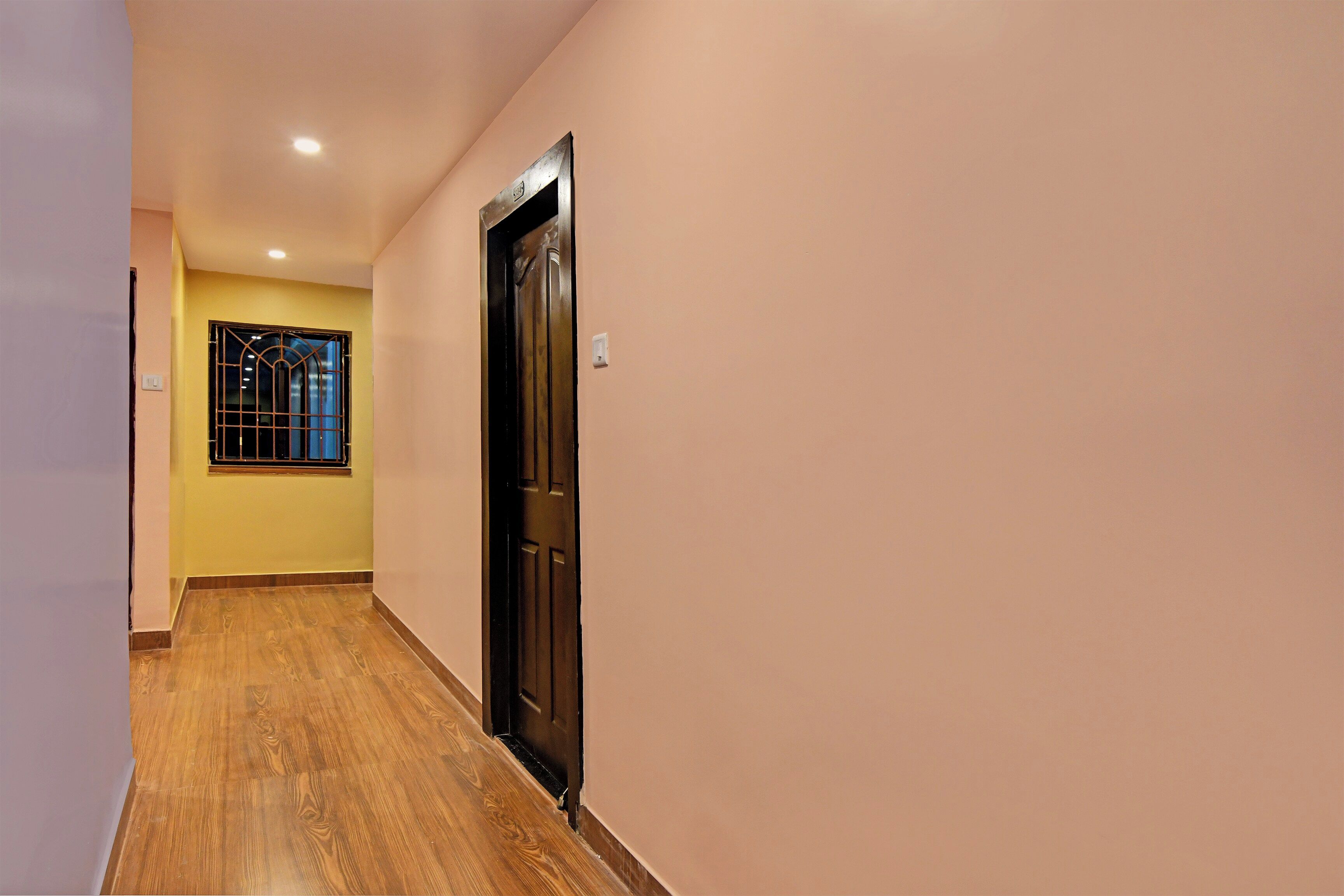 A hallway with a wooden floor, a door, and a window with bars.