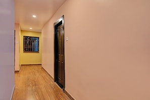 Un pasillo con piso de madera, una puerta y una ventana con barrotes.