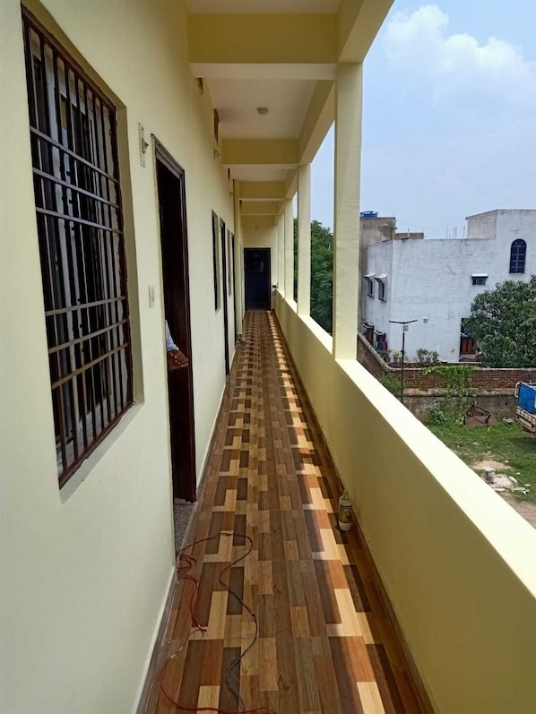 Un pasillo con piso estampado, ventanas con rejas y vistas a un edificio y vegetación al exterior.
