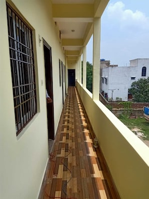 A corridor with a patterned floor, windows with metal bars, and a view of a building and greenery outside.
