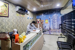 Una recepción con una persona sentada, un calendario y una pared decorativa con un mural de un paisaje urbano.
