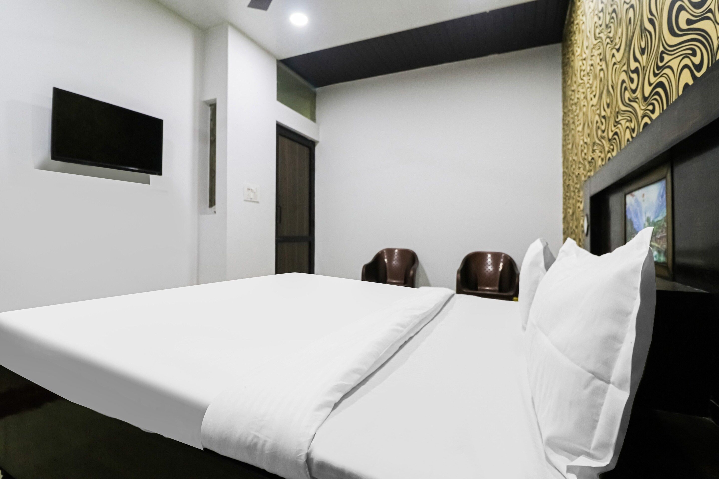 A hotel room with a single bed, a flat-screen TV mounted on the wall, and a decorative wall panel.
