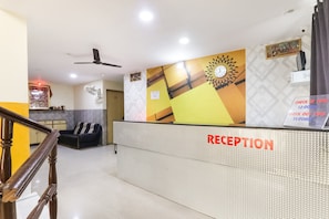 Un área de recepción con mostrador, ventilador de techo, reloj y señalización con los horarios de registro de entrada y salida.