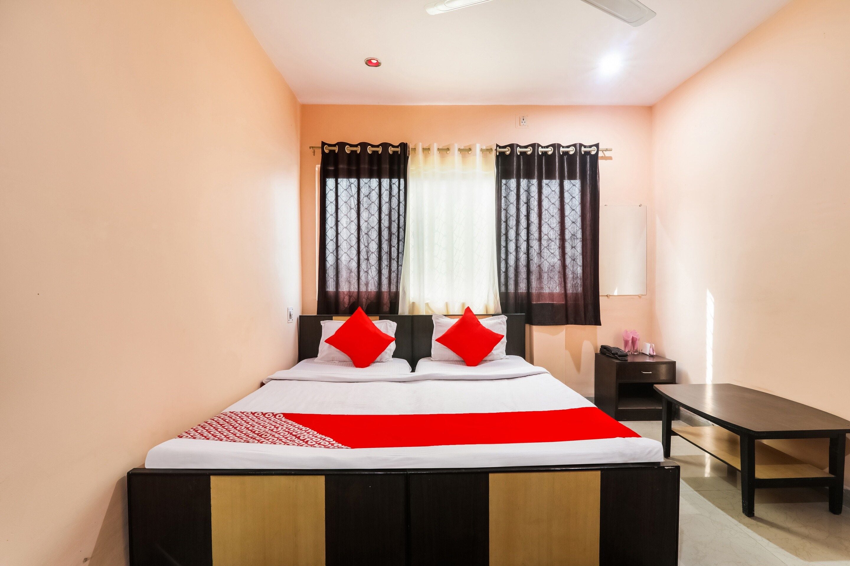 A hotel room with a bed, a bedside table, a desk, and a window with curtains.