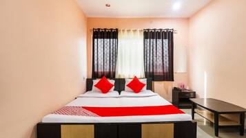 A hotel room with a bed, a bedside table, a desk, and a window with curtains.