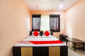 Una habitación de hotel con una cama, una mesita de noche, un escritorio y una ventana con cortinas.