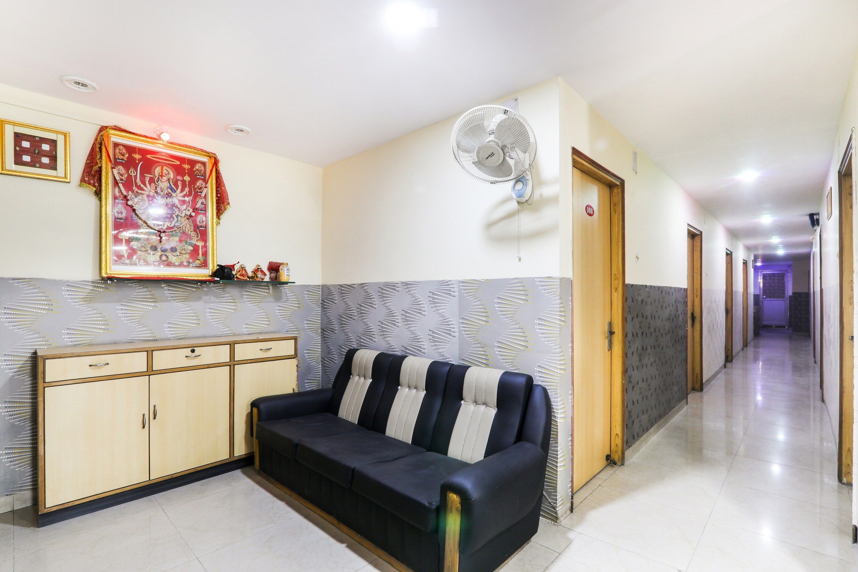 A hotel lobby with a sofa, a wall-mounted fan, a framed religious picture, and a patterned wall.