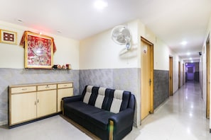 Un vestíbulo de hotel con un sofá, un ventilador de pared, un cuadro religioso enmarcado y una pared con diseño.