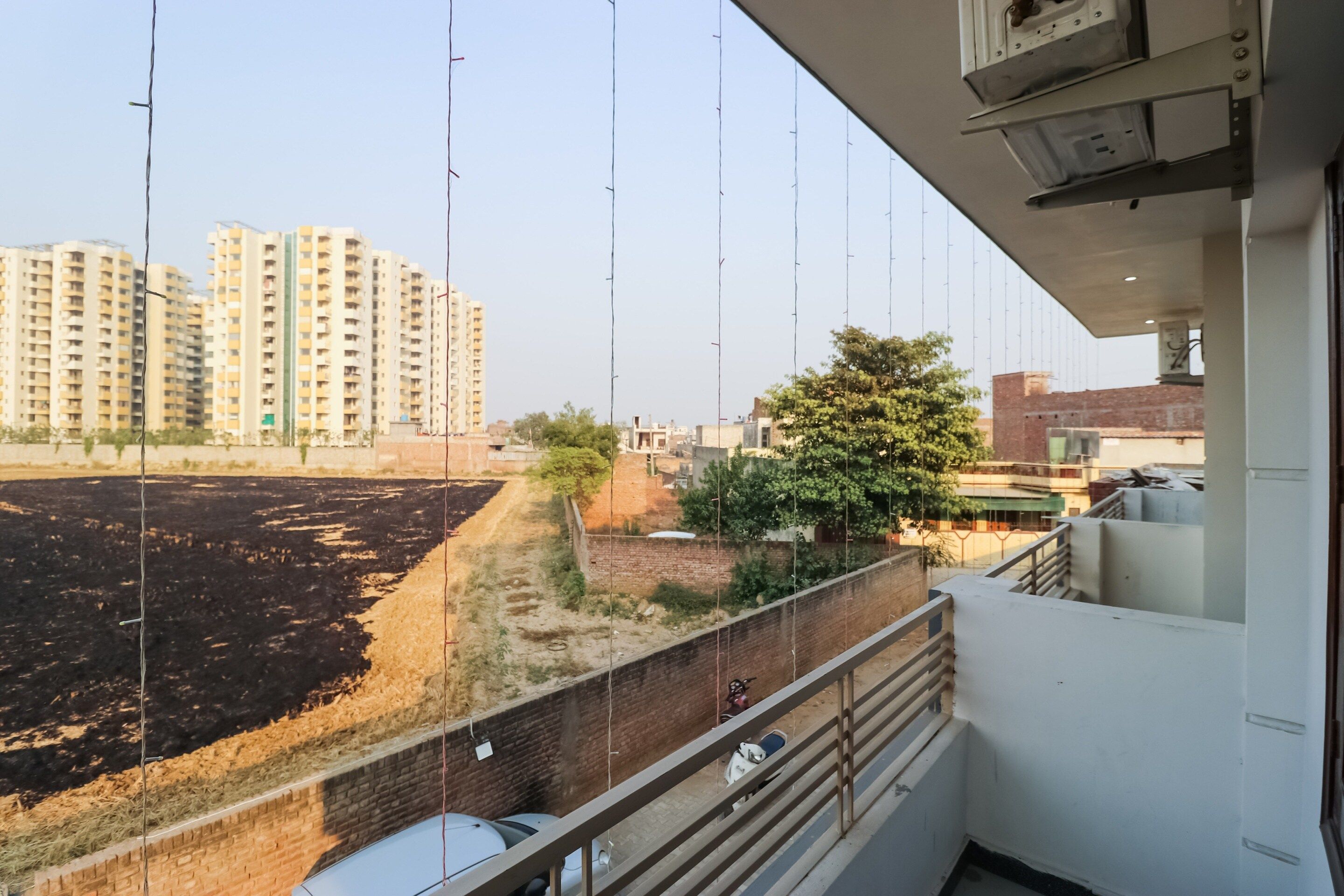 A balcony with a view of a construction site, a brick wall, and a tree.
