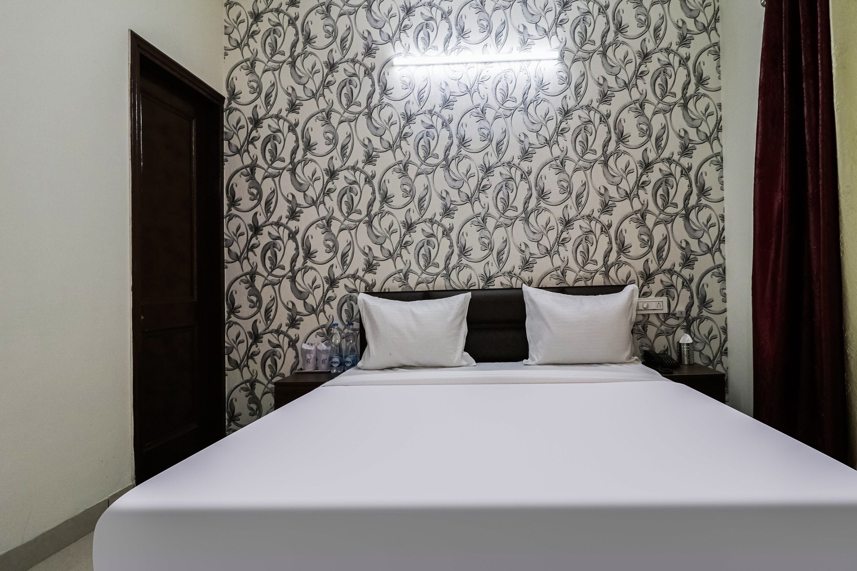 Habitación de hotel con cama, mesita de noche, lámpara y un papel tapiz floral.