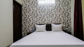 Habitación de hotel con cama, mesita de noche, lámpara y un papel tapiz floral.