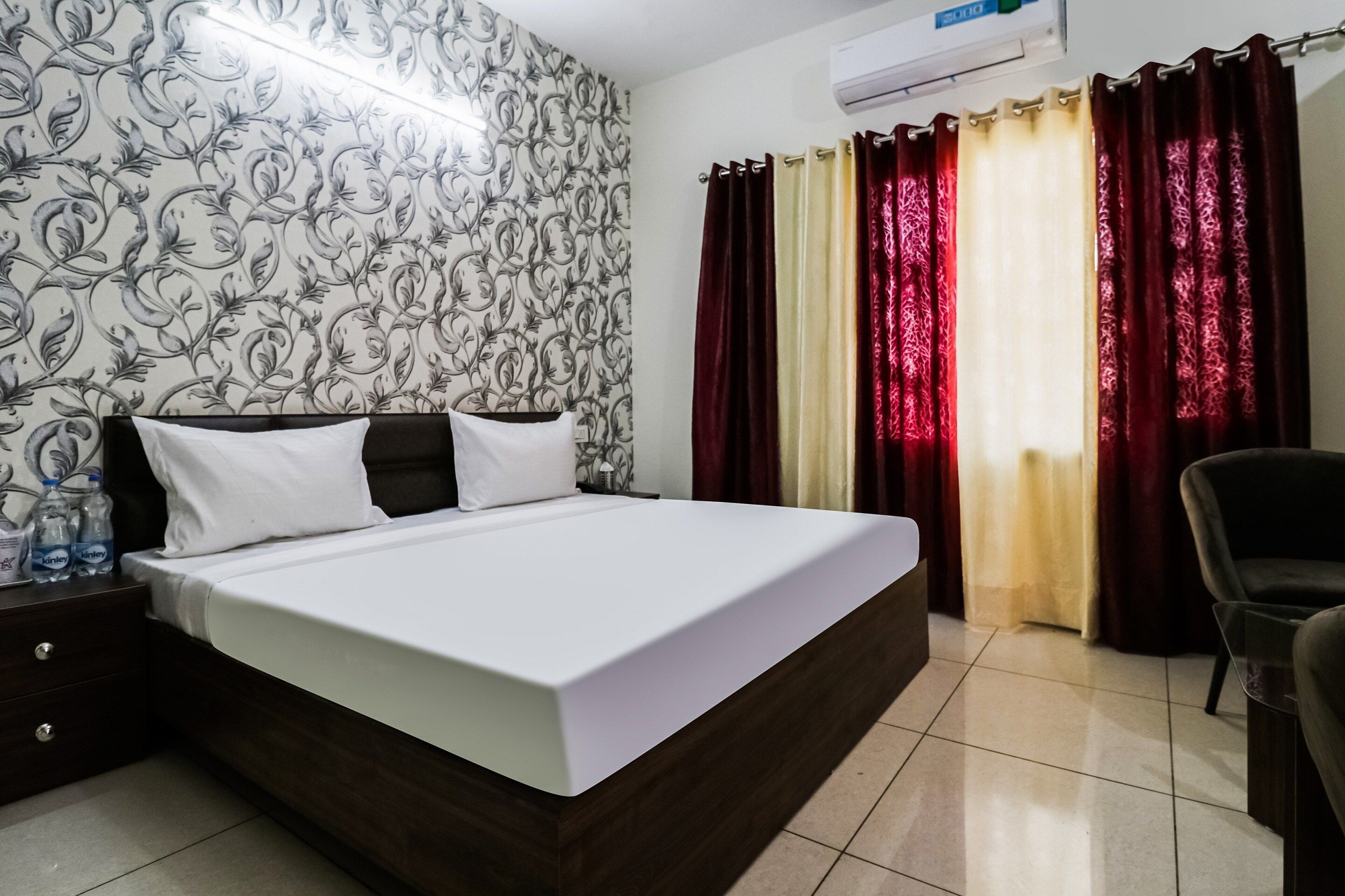 Une chambre d’hôtel avec un lit, une table de chevet, une chaise et une fenêtre avec des rideaux.
