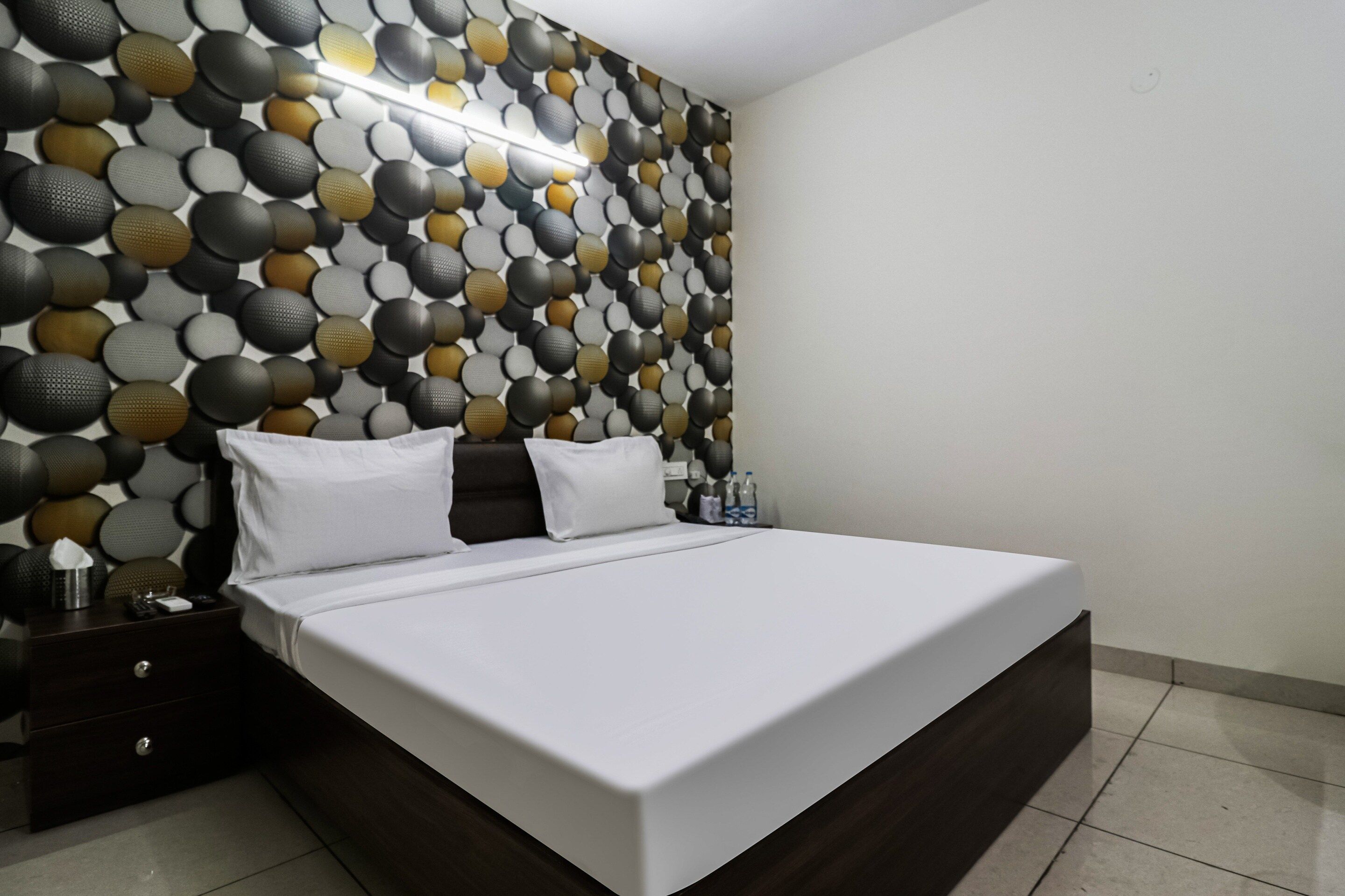 A modern bedroom with a large bed, a nightstand, and a wall with a textured pattern.