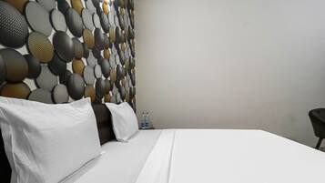 A hotel room with a neatly made bed, a headboard with a textured pattern, and a plain wall.