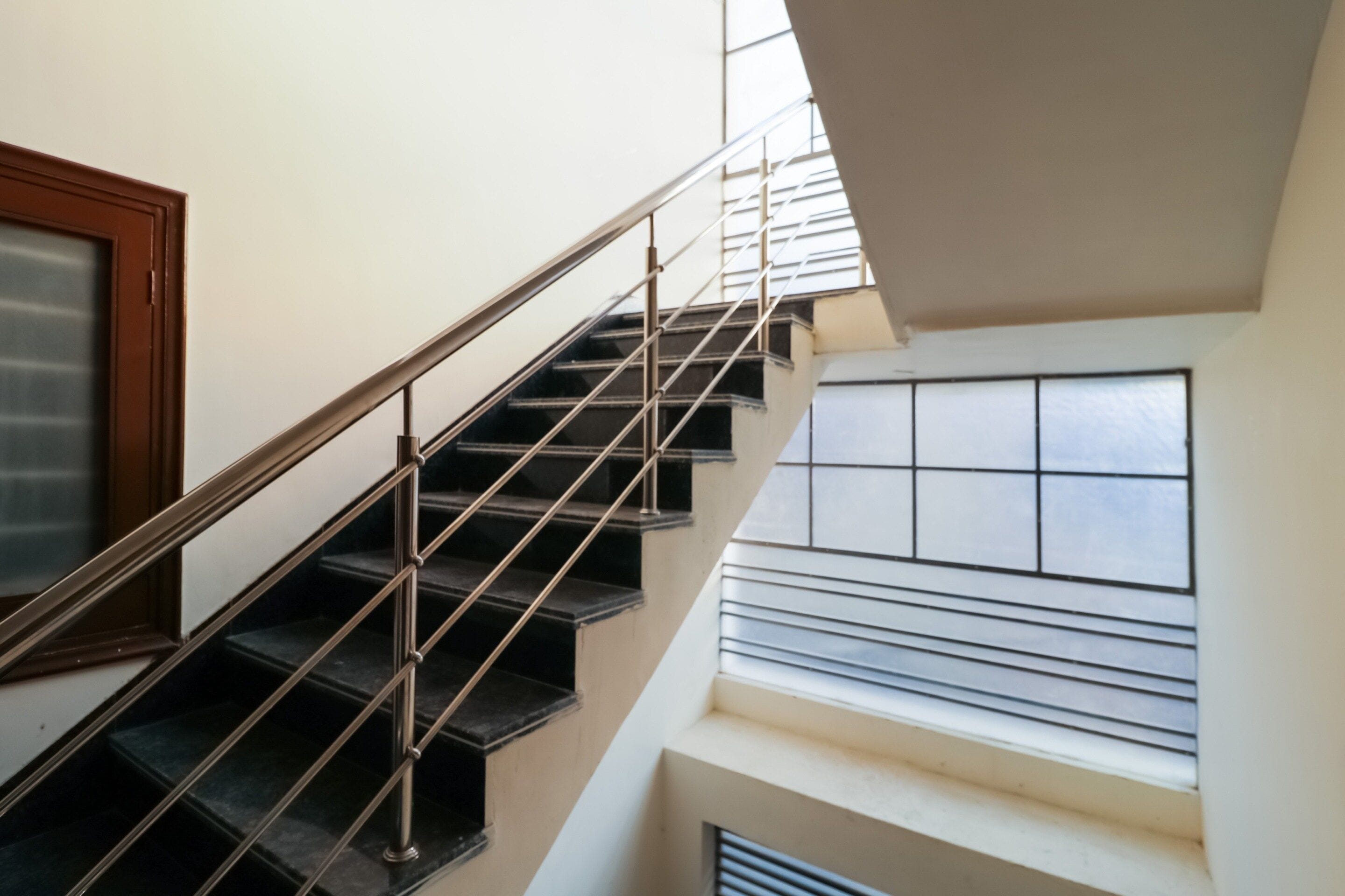 Una escalera con barandilla de metal que lleva a un rellano con ventana.
