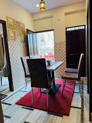 A dining area with a table and chairs, a red carpet, and a view of the outside. - Angan E Kashi (Varanasi)