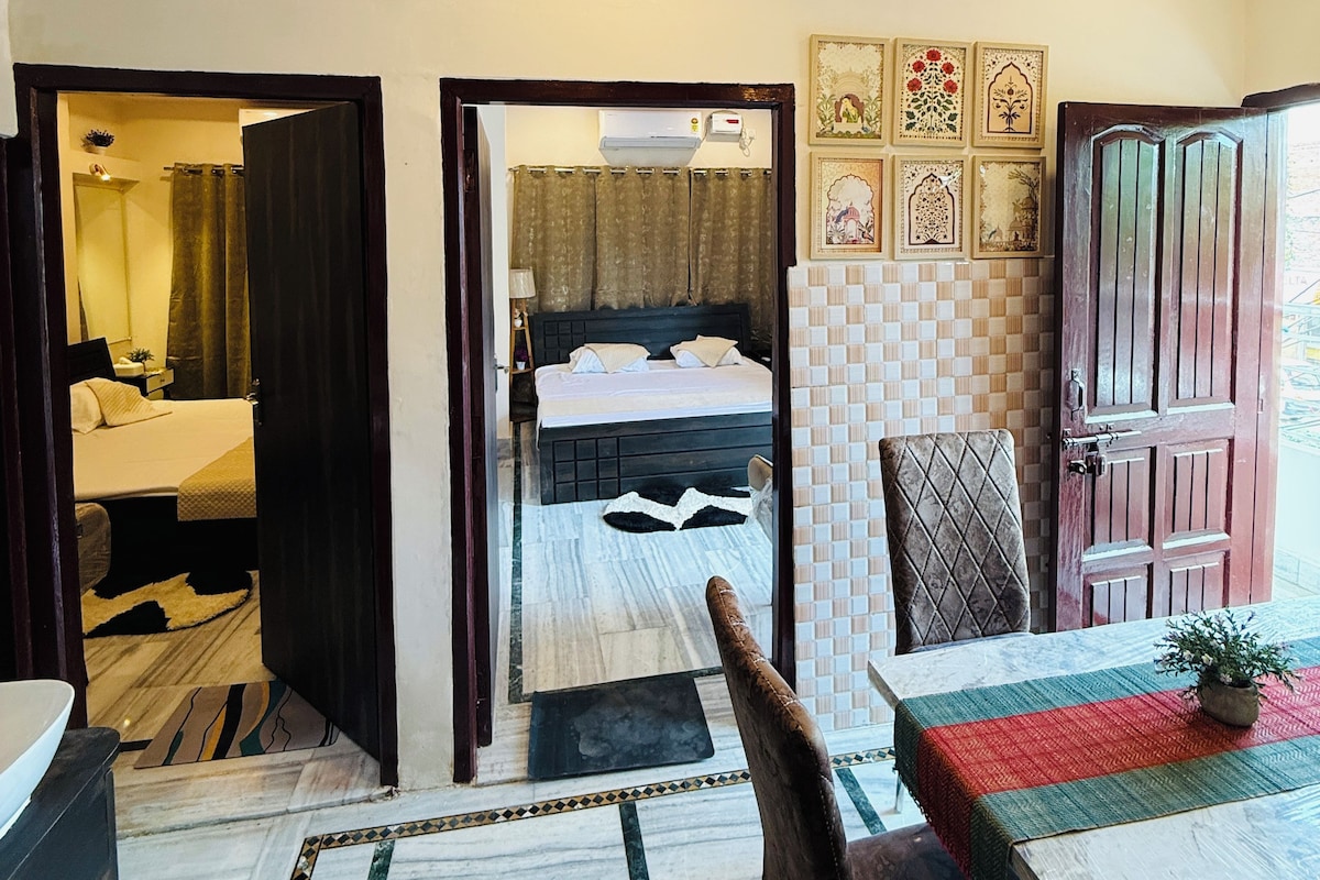 A hotel room with a bed, a bathroom, a dining area with a table and chairs, and a hallway leading to another room.