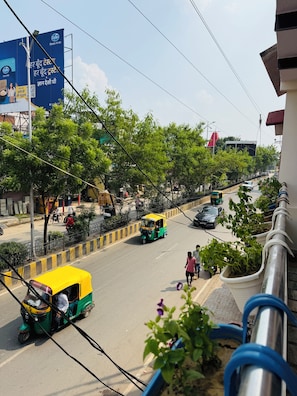 A street scene with auto-rickshaws, pedestrians, and greenery. - Angan E Kashi (Varanasi)