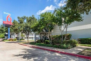 A hotel with a sign for 'studio 6 extended site' and a parking lot with trees and a sidewalk. - 1 Queen Bed|Non-smoking (Dallas)