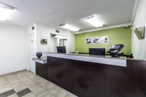 A reception area with a dark reception desk, a computer, and a green wall with framed pictures. - 1 Queen Bed | Smoking (Dallas)