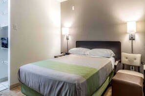 A hotel room with a bed, bedside table, lamp, and a chair. - 1 Queen Bed | Smoking (Dallas)