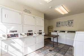 A laundry room with multiple washing machines and dryers, a table, and a sign indicating Studio 6 is not responsible for items. - 1 Queen Bed | Non-Smoking (Dallas)
