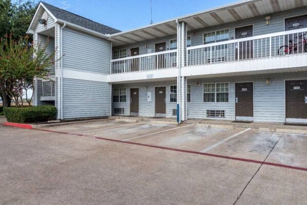 A two-story motel with a covered parking area and a small garden. - 1 Queen Bed | Non-Smoking (Dallas)