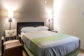 A hotel room with a bed, a chair, and two wall-mounted lamps. - 1 Queen Bed | Non-Smoking (Dallas)