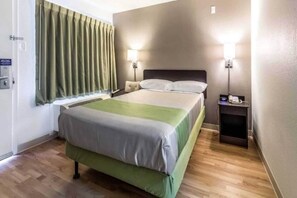 A hotel room with a bed, bedside tables, and a window with curtains. - 1 Queen Bed | ADA/RI Shower| NS (Dallas)