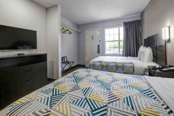A hotel room with a bed, a desk, a chair, a television, and a window. - 2 Full Beds | ADA/Roll-In Shower, Smoking (Arlington)