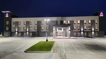 A multi-story hotel with a central entrance, parking lot, and illuminated signage.