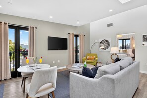 A modern living room with a grey sofa, a round coffee table, and a flat-screen TV mounted on the wall. - Wine Country Retreat • Walk To Downtown + Tasting Rooms | The Agave Room (Paso Robles)
