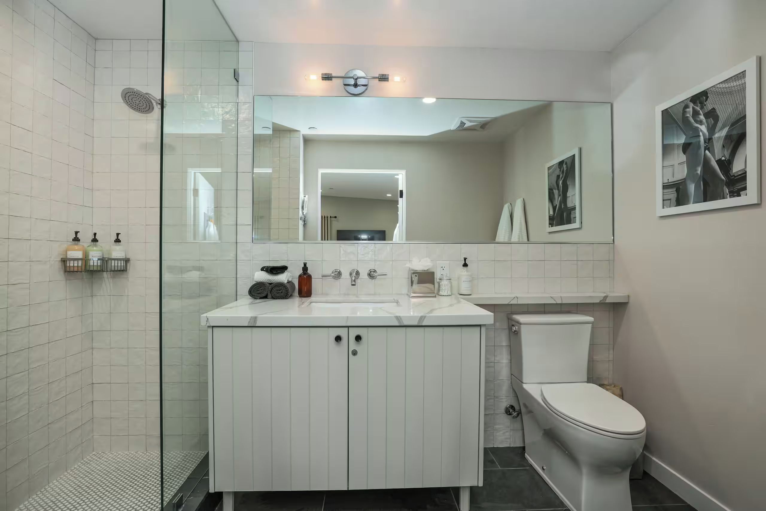 Un baño moderno con cabina de ducha de vidrio, un tocador blanco con espejo y un inodoro.
