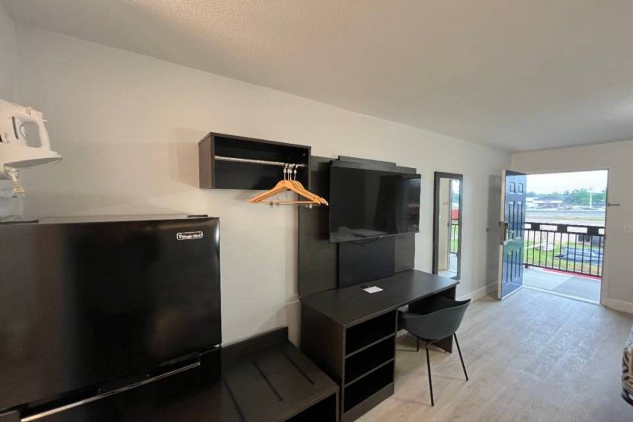 Une chambre moderne dotée d’un téléviseur à écran plat fixé au mur, d’un meuble de rangement noir, d’un bureau avec une chaise et d’un balcon offrant une vue agréable.