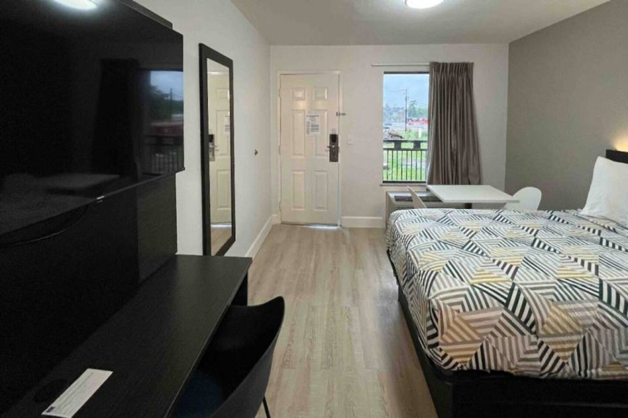 Ett hotellrum med en säng, ett skrivbord, en stol, en tv och en balkong med utsikt.