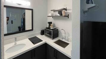 A modern bathroom with a large mirror, two sinks, a coffee machine, and a towel rack.