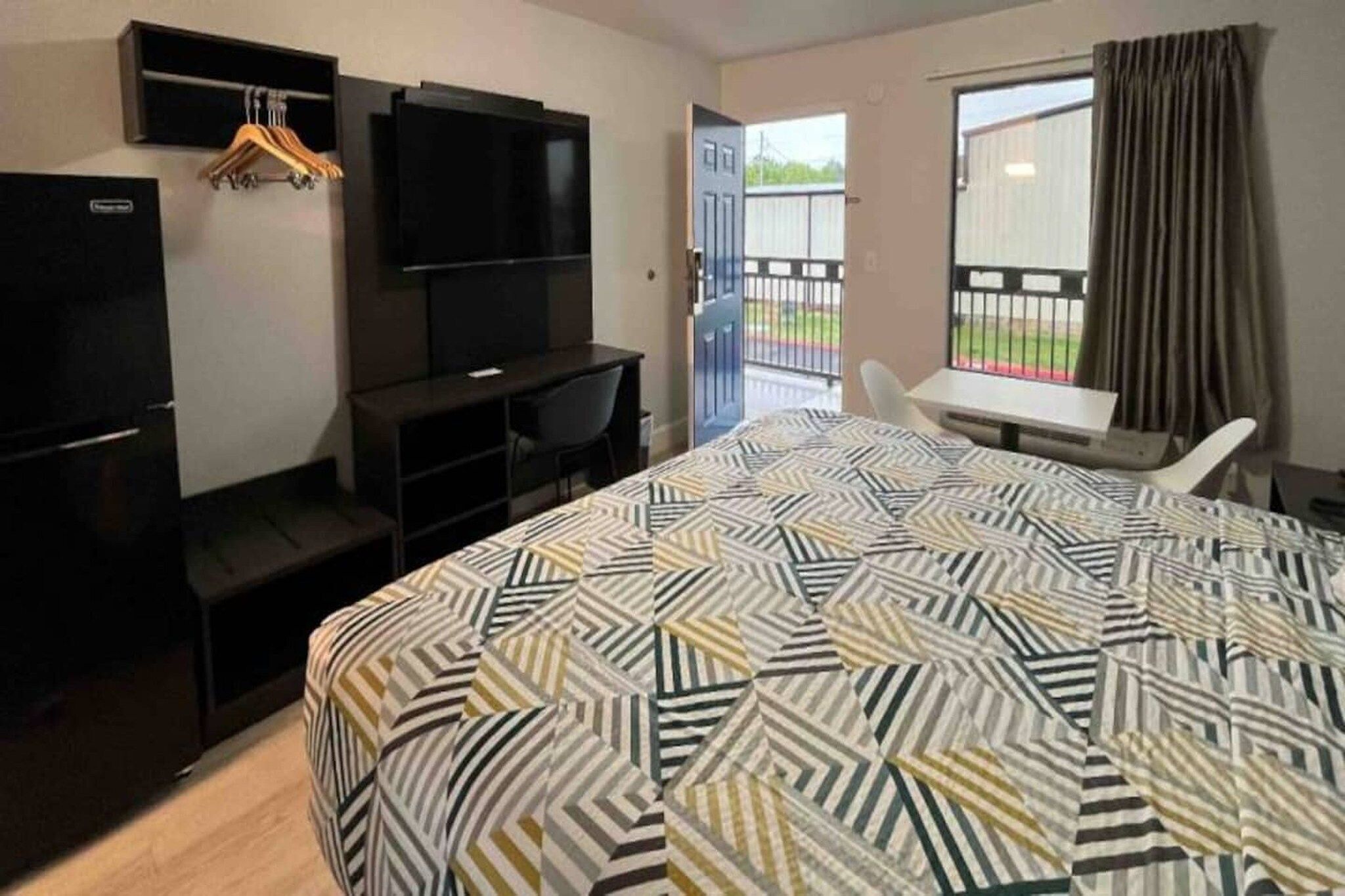 Ett hotellrum med en säng, ett skrivbord, en stol, en tv och ett fönster med gardiner.