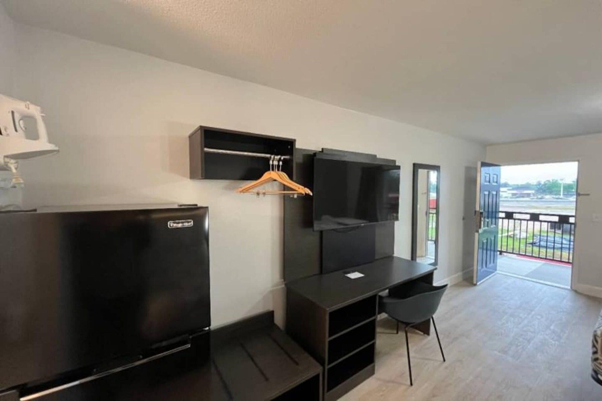 A modern room with a flat-screen TV, a black refrigerator, a desk, and a chair.
