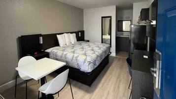 A hotel room with a bed, a desk, a chair, a kitchenette, and a bathroom.