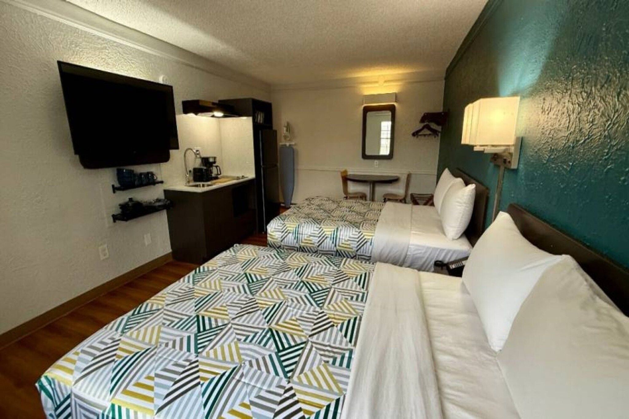 A hotel room with two beds, a desk, a television, and a mirror.