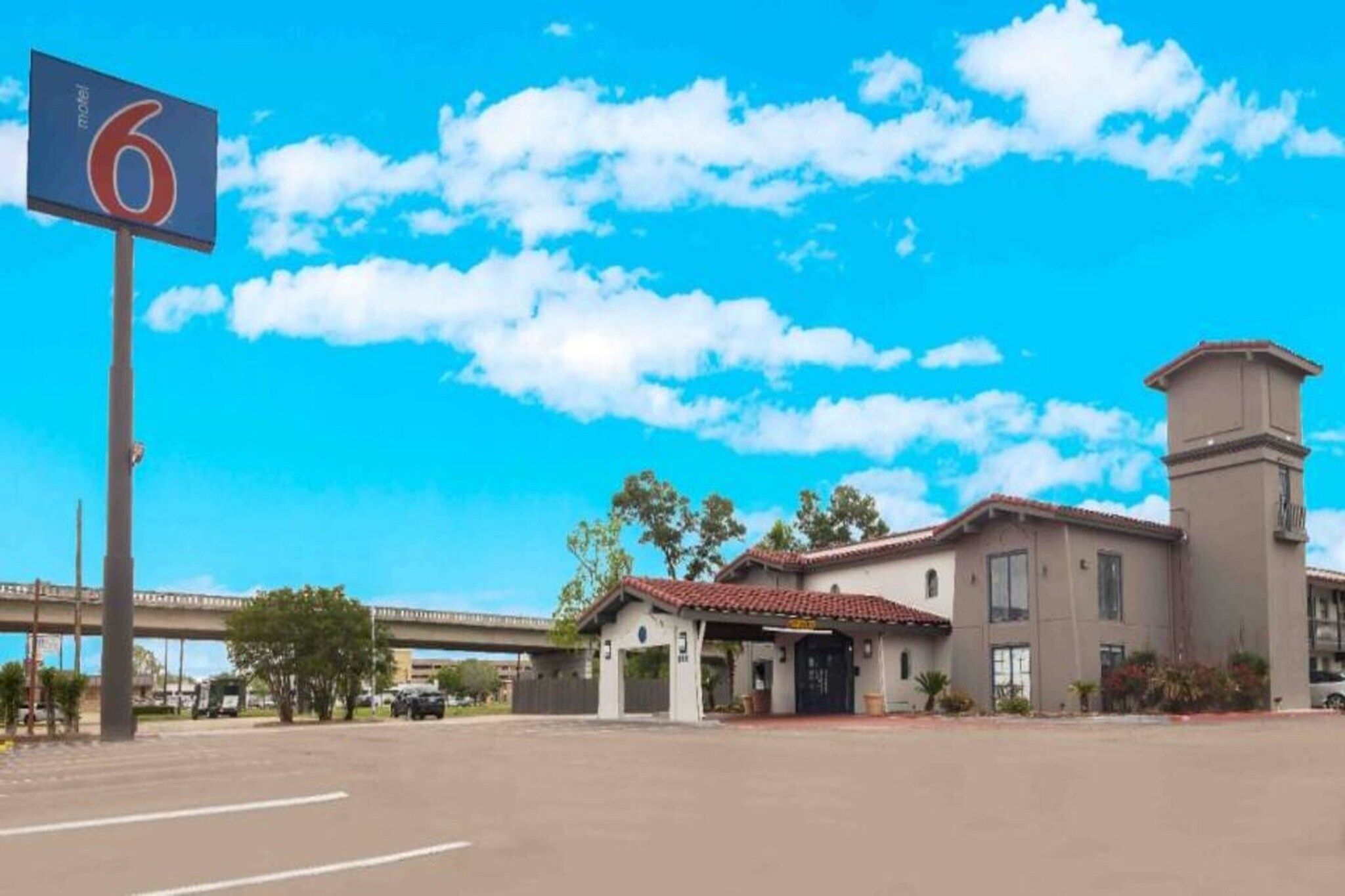 A motel with a clear blue sky, a parking lot, and a bridge in the background.