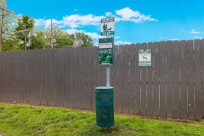 Un espace dédié aux déjections canines, comprenant un panneau indiquant qu’il faut ramasser les excréments de son chien, une clôture et une zone herbeuse.