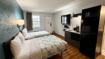 A hotel room with two beds, a kitchenette, a refrigerator, and a window with curtains.