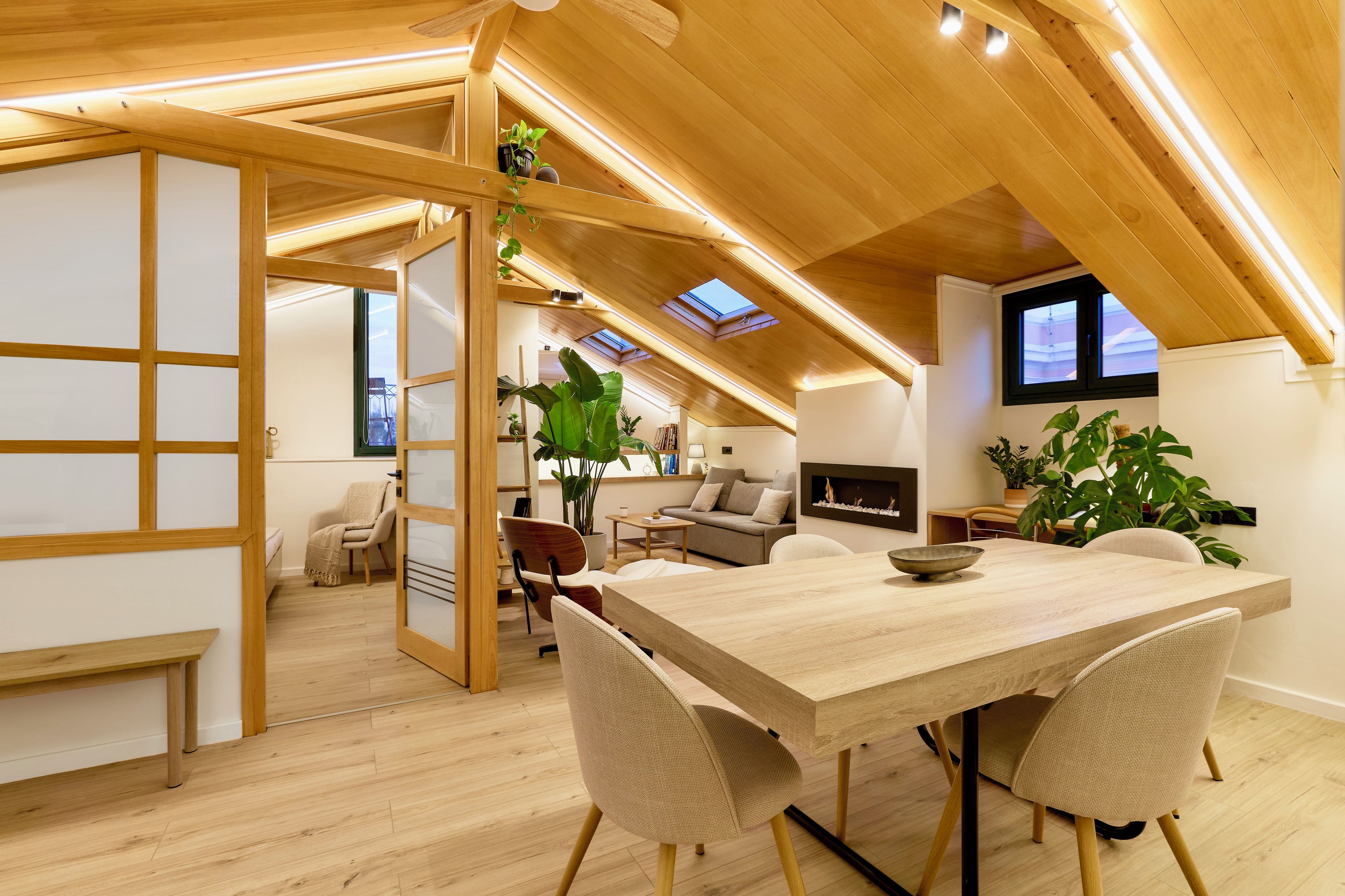 A spacious loft with a high ceiling, wooden beams, a dining area with a long table, and a cozy seating area with a sofa and chairs.