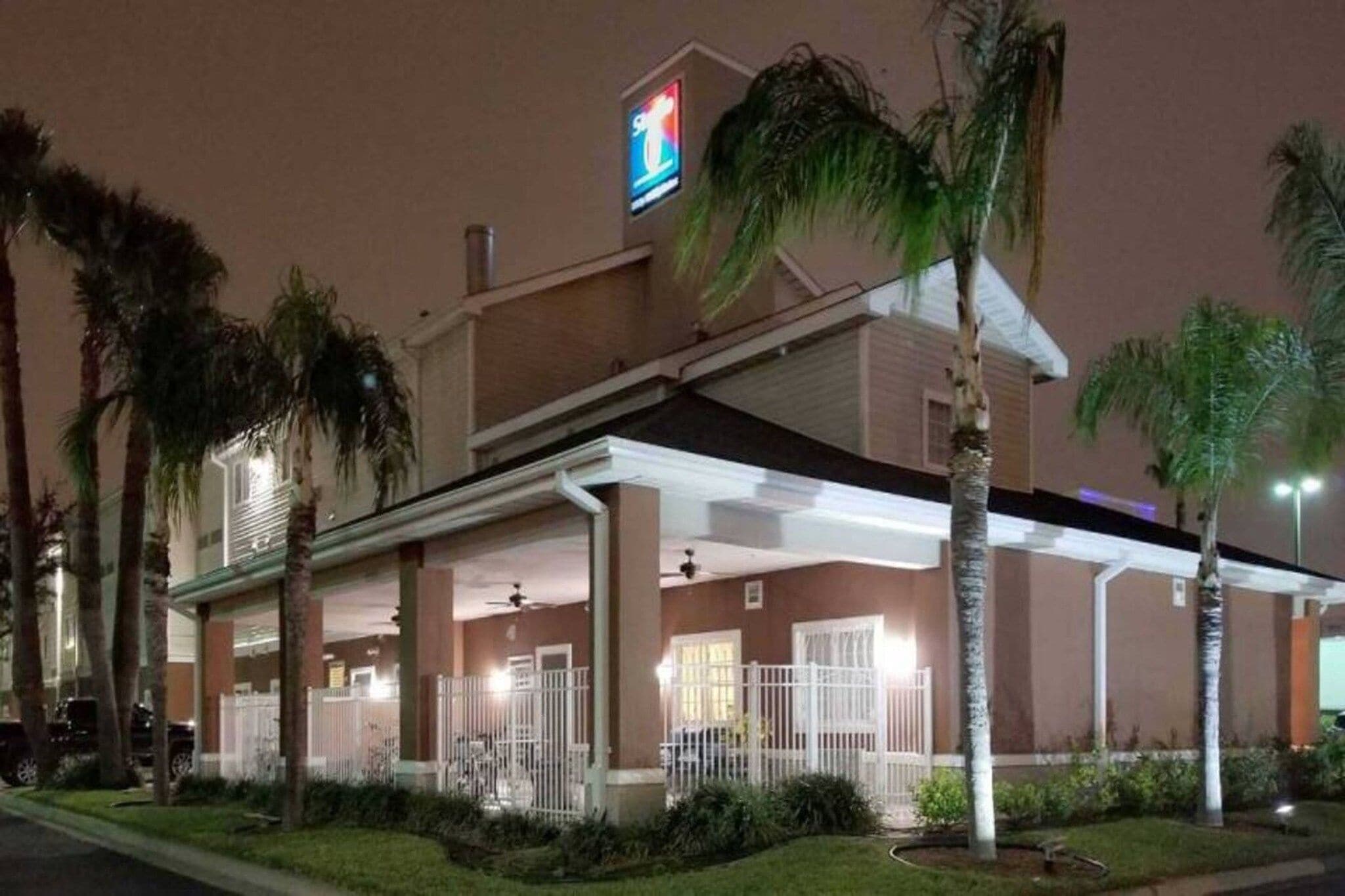 A hotel with a covered outdoor area, palm trees, and a sign indicating a restaurant.